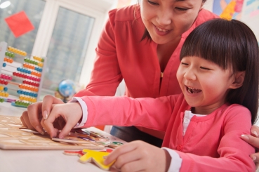 Teacher Helping Young Girl with Cut-Out Alphabet Letters