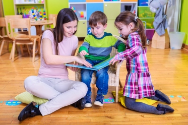 Kindergarten teacher reads a book to children at school