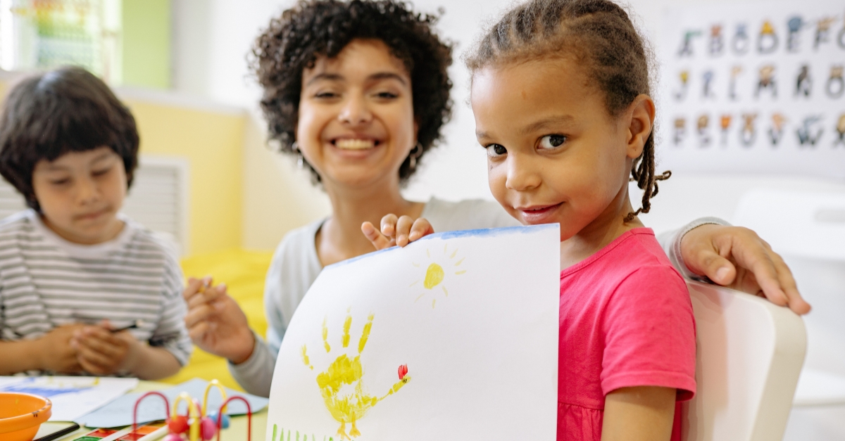 Preschooler with teacher holding up a craft creating in their center 